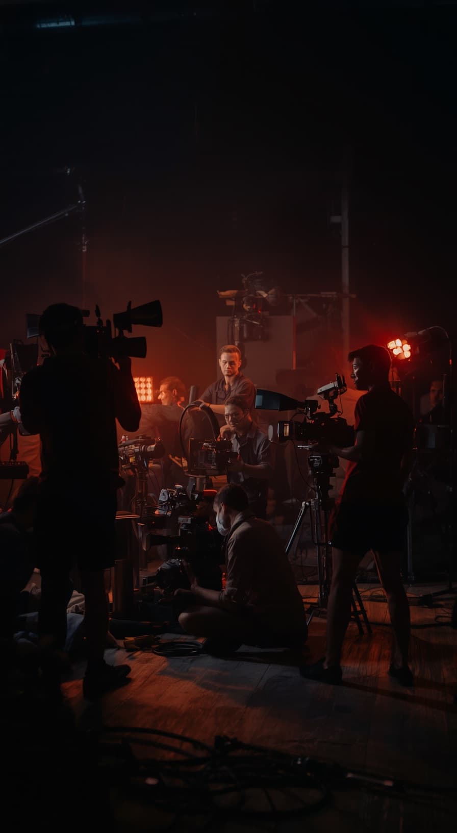Equipe de filmagem em um set, com câmeras e luzes vermelhas ao fundo